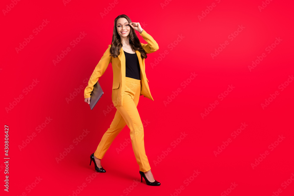 Photo of sweet pretty young lady dressed yellow blazer glasses holding modern device empty space isolated red color background Photo of sweet pretty young lady dressed yellow blazer glasses holding modern device empty space isolated red color background