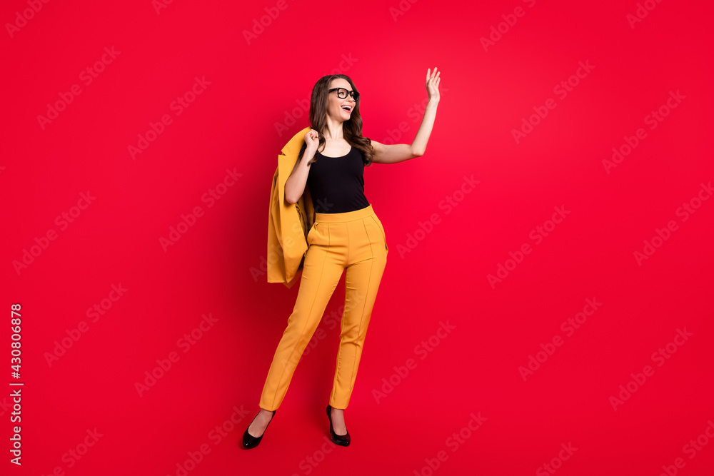 Photo of pretty charming young woman wear yellow jacket spectacles waving arm empty space smiling isolated red color background