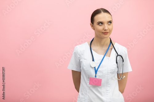A smiling lady doctor in a white apron stands against a pink background.