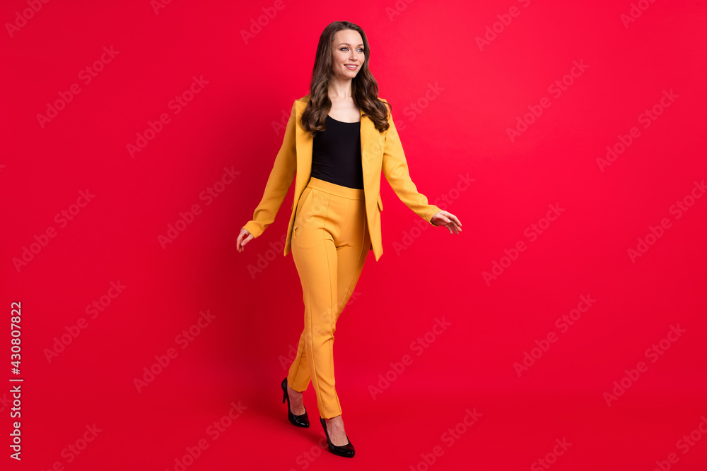 Full length photo of happy charming nice young woman look go empty space smile isolated on red color background Full length photo of happy charming nice young woman look go empty space smile isolated on red color background