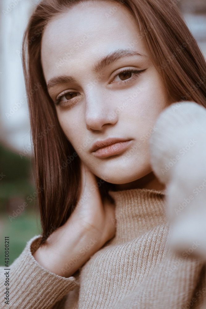 Portrait of a woman. Young girl. A brunette in a yellow sweater looks into the camera. Hands near the neck Portrait of a woman. Young girl. A brunette in a yellow sweater looks into the camera. Hands near the neck