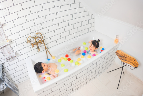 A boy and a girl lie in a bath filled with foam and colored balls. Kids relax and have fun in bathroom. Top view.