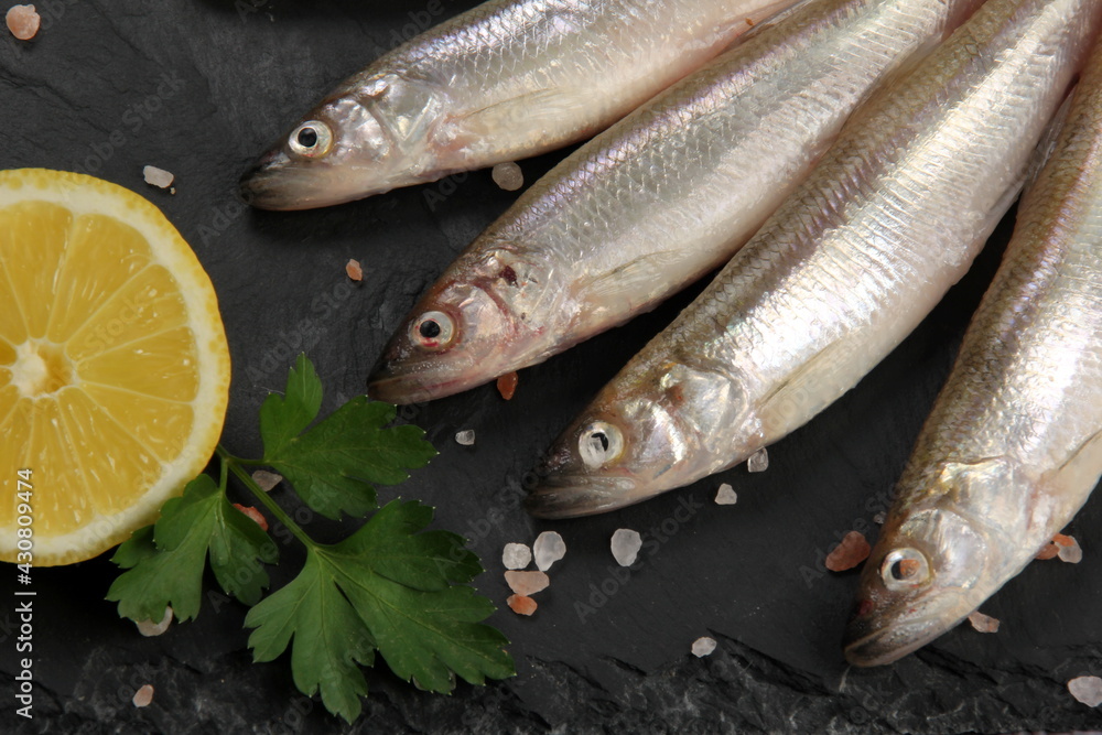 Fresh smelt fish on a black stone plate, Smelt fishes (European smelt) with lemon and green parsley, Group of fresh smelt fish Fresh smelt fish on a black stone plate, Smelt fishes (European smelt) with lemon and green parsley, Group of fresh smelt fish