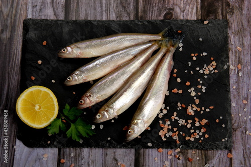 фотографія Fresh smelt fish on a black stone plate, Smelt fishes (European smelt) with lemo