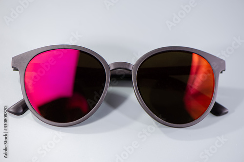 Dark sunglasses and orange and red reflections in glasses lie on a light background.