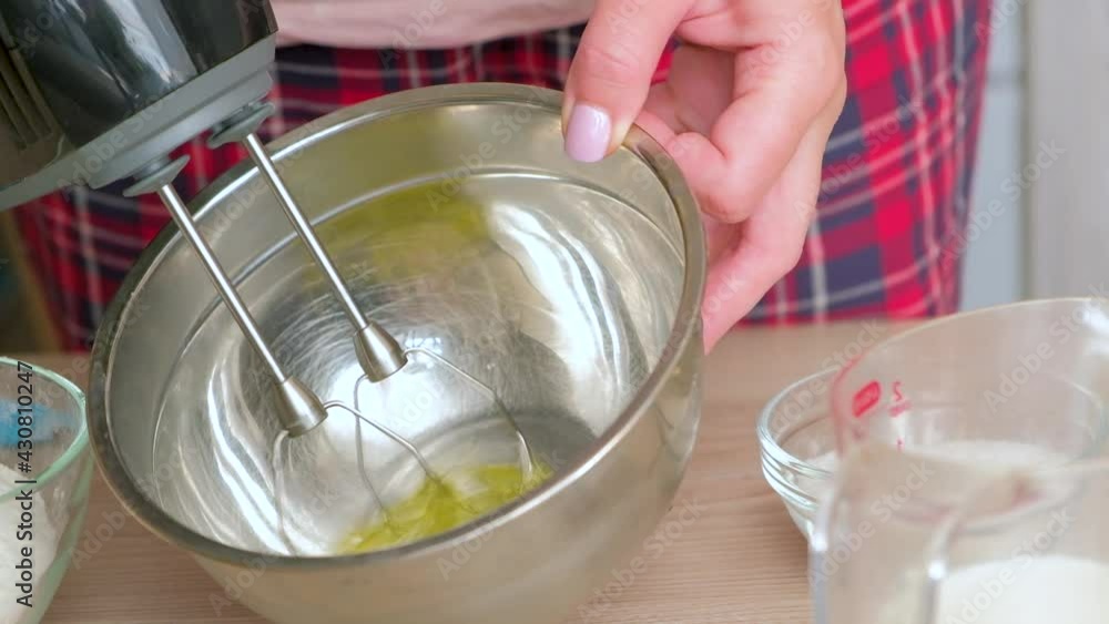 Woman with kitchen mixer whips egg whites. Electric mixer beats. Female hand holds iron bowl. Chicken egg for tasty dish. Woman with kitchen mixer whips egg whites. Electric mixer beats. Female hand holds iron bowl. Chicken egg for tasty dish.