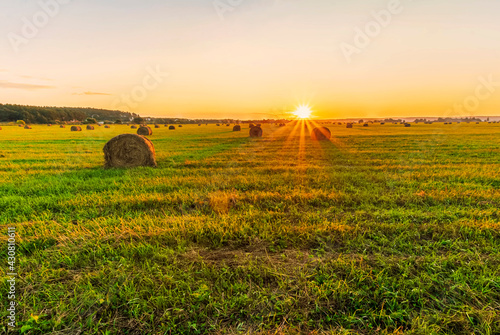 Scenic view at beautiful sunset in a green shiny field in willage farm with hay stacks, cloudy sky, golden sun rays, anazing summer valley evening landscape