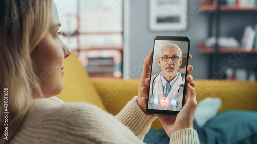 Close Up of a Female Chatting in a Video Call with Her Senior Family Doctor on Smartphone from Living Room. Ill-Feeling Woman Making a Call from Home with Physician Over the Internet. photo