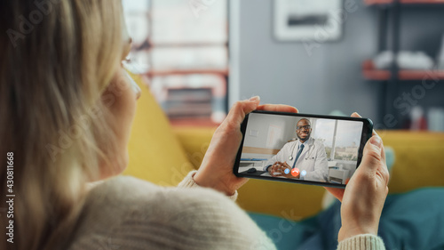 Close Up of a Female Chatting in a Video Call with Her Male Family Doctor on Smartphone from Living Room. Ill-Feeling Woman Making a Call from Home with Physician Over the Internet. Horisontal Vew. photo