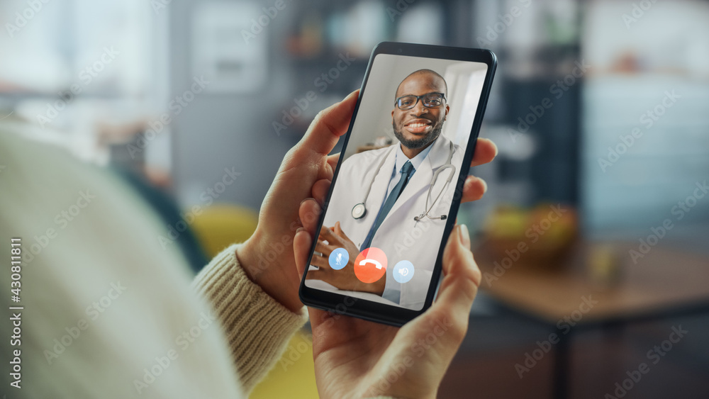 © Gorodenkoff - Close Up of a Female Has a Video Call with Her Female Family Doctor on Smartphone from Living Room. Ill-Feeling Woman Making a Call from Home with Physician Over the Internet.