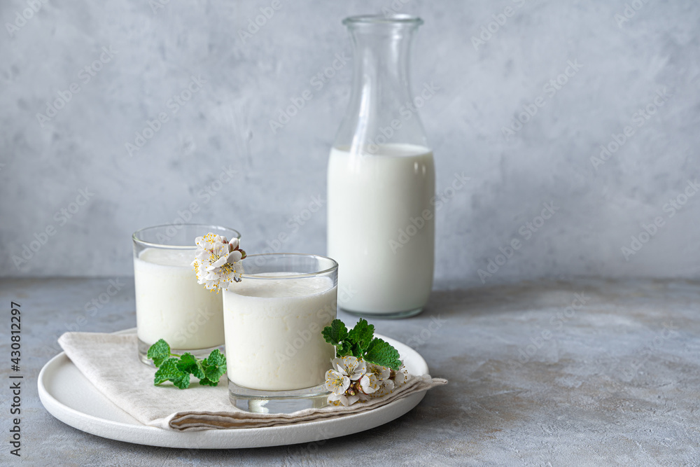 Natural, healthy milk drink-yogurt, kefir, lassi, in two glasses on a gray background with greenery and flowers. Natural, healthy milk drink-yogurt, kefir, lassi, in two glasses on a gray background with greenery and flowers.