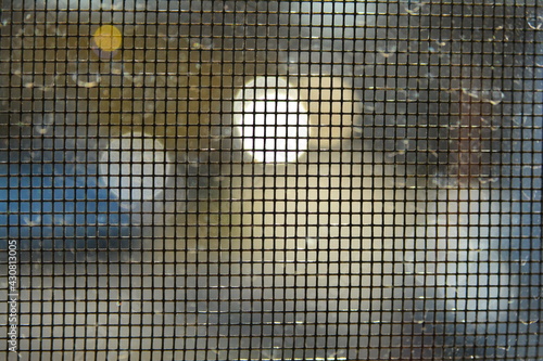 Macro image of window screen with out of focus lights outside creating distorted light shapes.