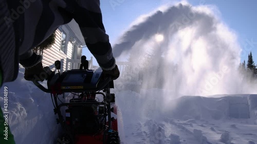 Close up shooting from behind of a mechanical snowplough being pushed by a young man to clear a path from the snow in residential complex.