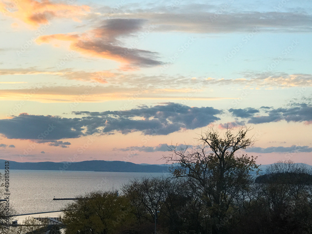 Sunset over Lake Champlain in Burglington, Vermont, with dark trees in the foreground.  Mountains are in New York State.