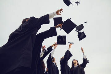 New stage of life. Graduates toss their academic hats into the sky during a solemn ceremony at the university. Students make a gesture of successful graduation. Education, graduation and alumni.