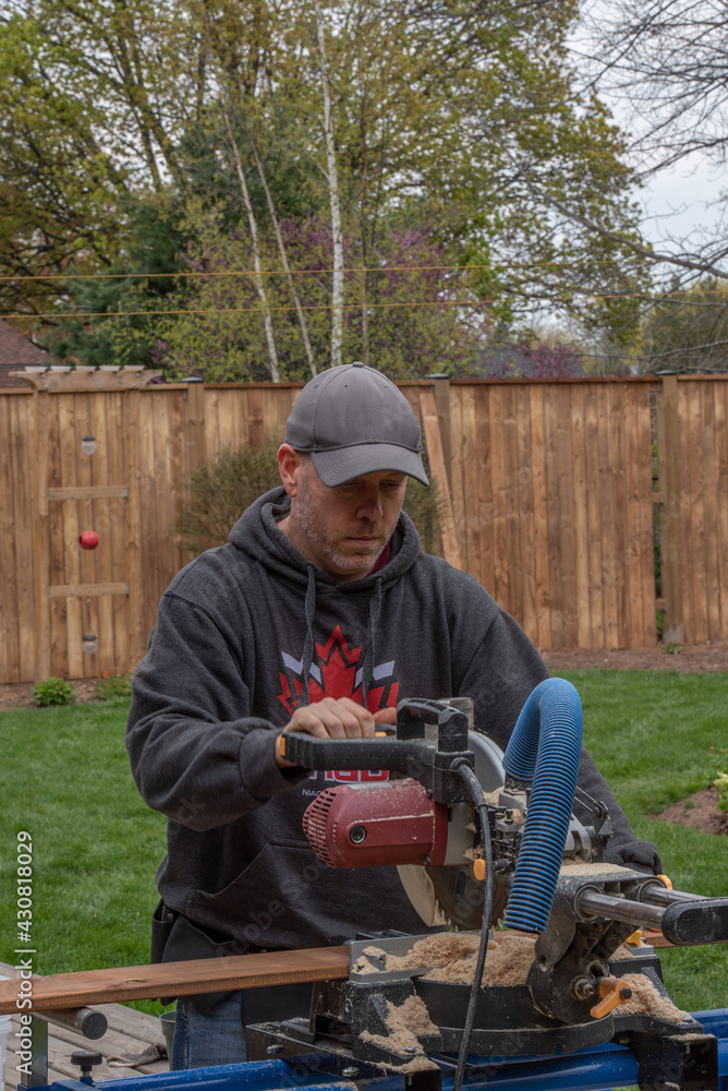 A white, middle-aged gay man builds a wooden fence in his back yard. A white, middle-aged gay man builds a wooden fence in his back yard.