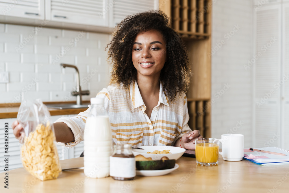 The happy woman taking a package of cereal while sitting at the table in the kitchen