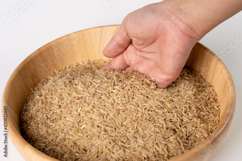 Raw brown rice in a woman's hand on a wooden bowl with raw brown rice.