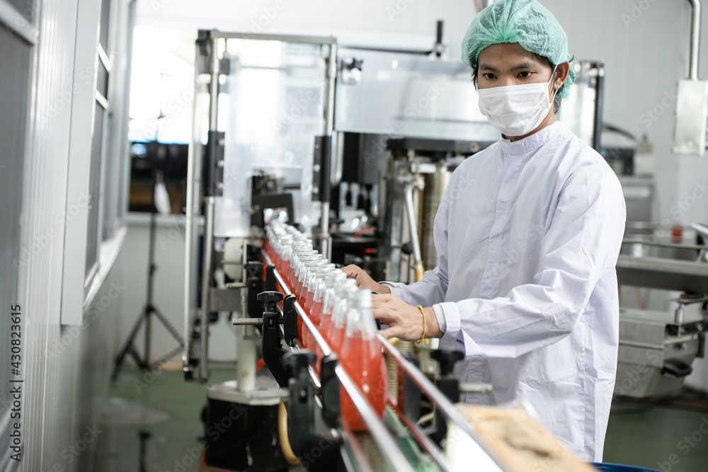 Hygiene worker working in drink factory at conveyor belt with fruit juice glass bottled in production line.
