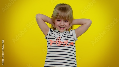 Little blonde teen kid child girl in t-shirt celebrate success win scream rejoices doing winner hands gesture say Yes, dancing isolated on yellow studio background. Young children lifestyle emotions