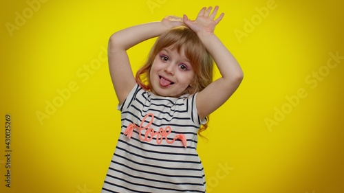 I am little bunny rabbit. Lovely funny teen kid child girl smiling friendly and doing bunny ears gesture on head, having fun, fooling with humorous comical mood. Young children on yellow background