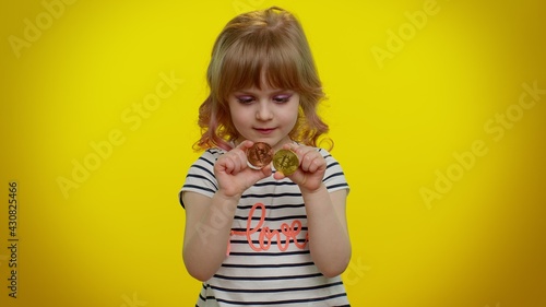 Portrait of funny blonde child girl 5-6 years old showing golden bitcoins. Achievement career wealth, cryptocurrency investment, mining, future technology. Teen kid children on yellow wall background © Andrii Iemelianenko