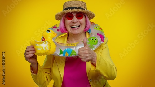 Traveler tourist senior stylish granny woman play with swimming ring and inflatable duck toy, ready for travel on weekends. Summer vacation, journey trip to seaside. Elderly grandmother on orange wall
