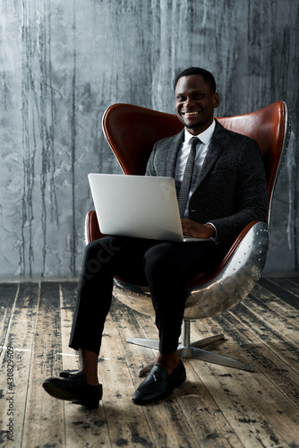 Happy african american office worker smiling while sitting on chair and working on laptop