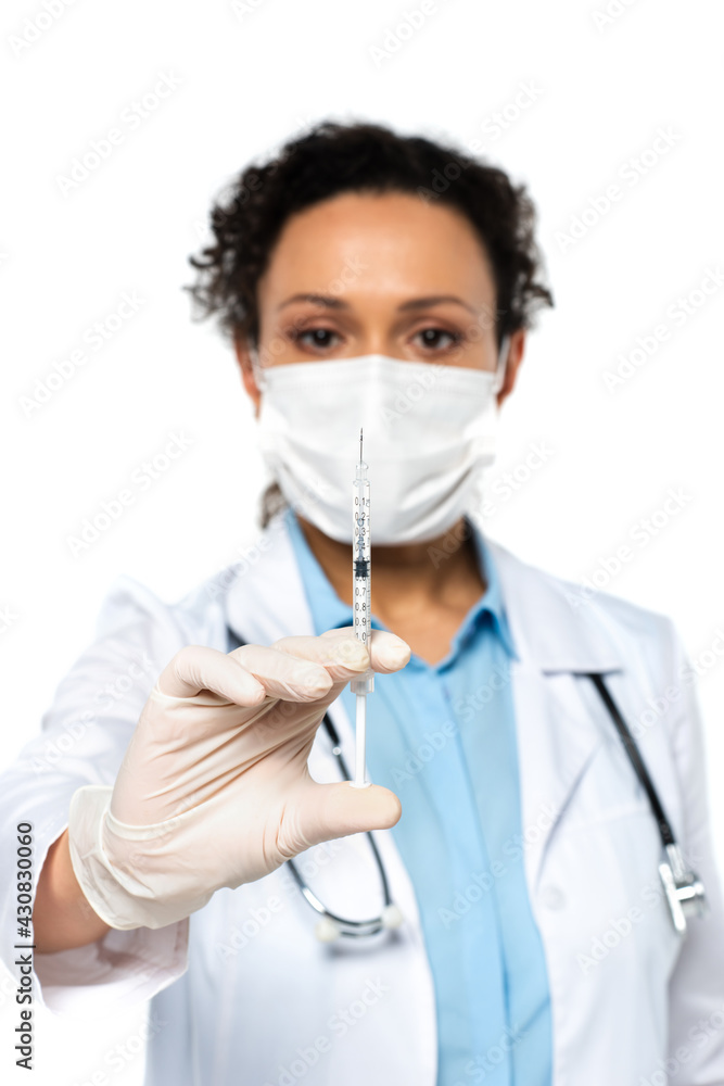 Syringe in hand of african american doctor in medical mask on blurred background isolated on white
