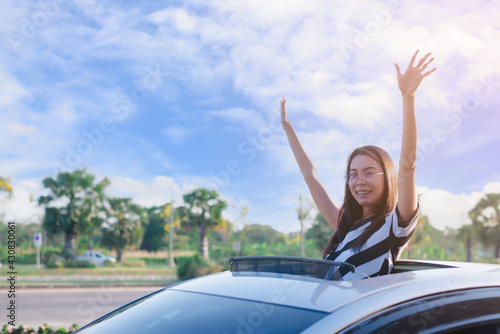 Young woman putting his hands out of the car sunroof top, driving down a country road,relaax vacation time concept.