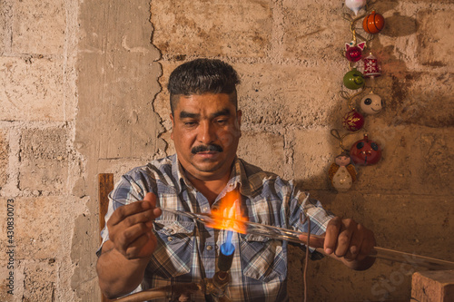 Craftsman blowing glass to create Christmas balls in his workshop, with the help of a blowtorch he shapes the glass tubes to turn them into spheres of different shapes. photo