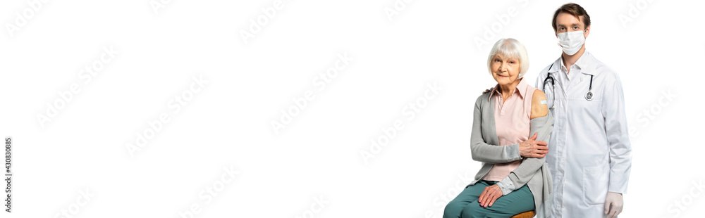 Senior woman with adhesive plaster smiling near doctor in medical mask isolated on white, banner Senior woman with adhesive plaster smiling near doctor in medical mask isolated on white, banner