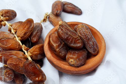 Dates (Phoenix dactylifera) on a wooden bowl on a whitecloth background. food for breaking the fast during Ramadan for Muslims. selective focus
