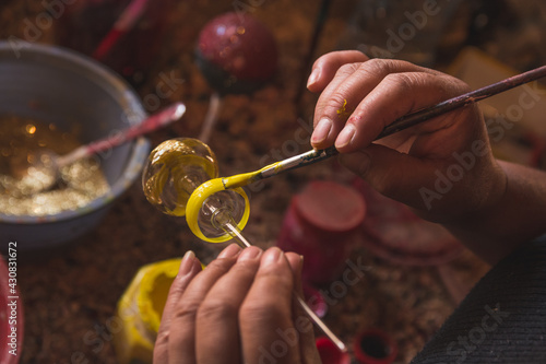 Craftsman painting Christmas spheres in his workshop in different colors, using acrylic paint, diamond paint to give texture and different figures.