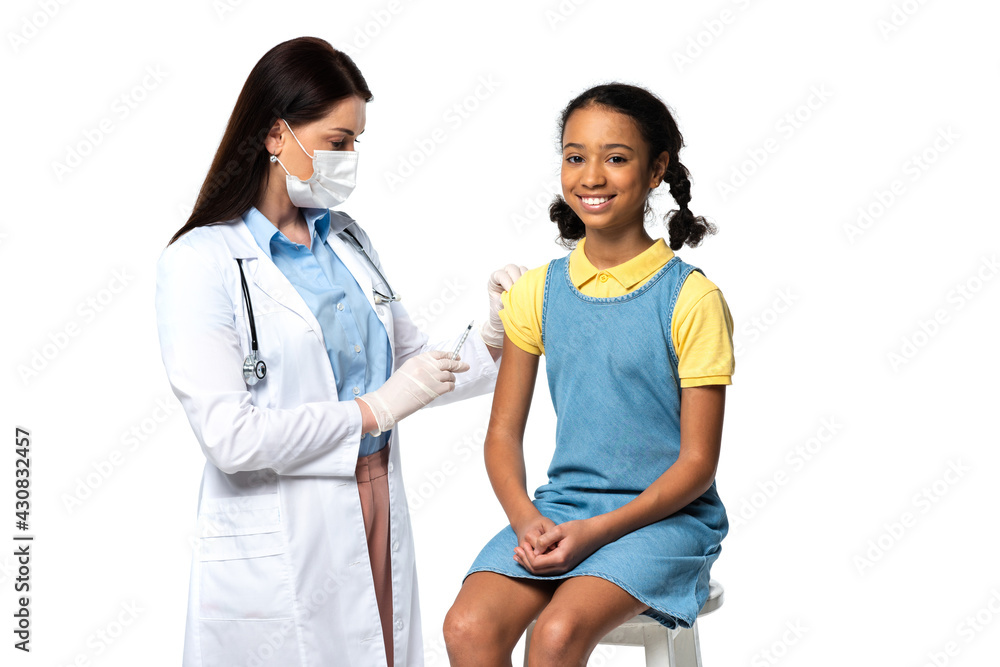 Doctor in medical mask holding syringe near cheerful african american kid isolated on white Doctor in medical mask holding syringe near cheerful african american kid isolated on white
