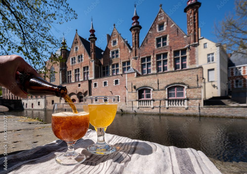 Naklejka premium Tasting of Belgian beer on open cafe or bistro terrace with view on medieval houses and canals in Bruges, Belgium