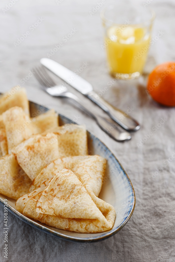 Breakfast with crepes or pancakes and jam, juice and tangerine on greige linen tablecloth. Pancake week or Shrovetide. Selective focus Breakfast with crepes or pancakes and jam, juice and tangerine on greige linen tablecloth. Pancake week or Shrovetide. Selective focus