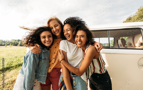 Fototapeta Four happy female friends laughing together standing in front of a van
