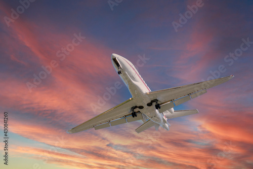 Airplane in the sky at sunrise or sunset. Small business jet is flying with lights and deployed landing gear preparing for landing or after takeoff.