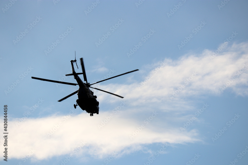 Military helicopter silhouette in flight on background of blue sky and white clouds. Bottom view, air transportation concept Military helicopter silhouette in flight on background of blue sky and white clouds. Bottom view, air transportation concept