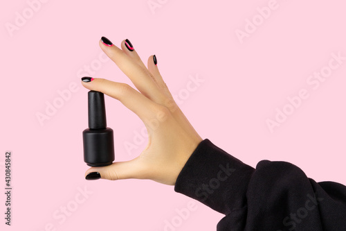 Womans hand with trendy manicure holding nail varnish on pink background
