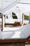 Wooden beach canopies covered by fabric on the beach of the Mediterranean Sea. White curtain being blow by wind. Comfortable chaise lounges on the zone of relaxation next to the pool, romantic place.