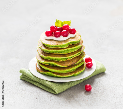 Vegan spinach pancakes with green matcha tea with berries on a plate on a light gray background