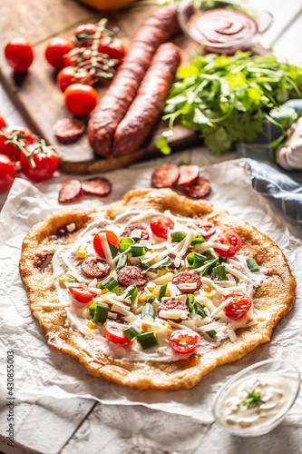 Traditional hungarian combo made of deep fried crusty langos with garlic edges, precisely served with cream, grated cheese, tomatoes and domestic sausages also with extra cream in little bowl