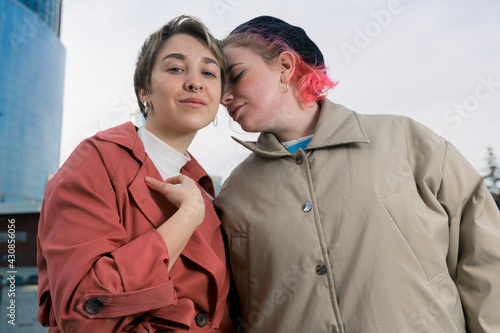 A young pair of lesbian girls sensually clung to each other standing on the street of the city against a clear sky. High quality photo