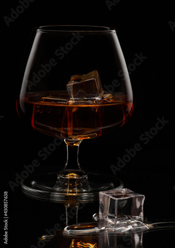 A lone glass with a noble drink, chilled with ice cubes, one fell out and began to melt.