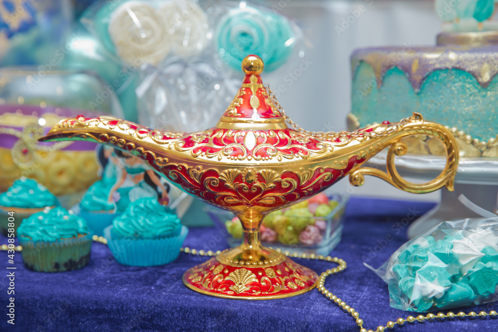 Aladdin lamp of wishes on table . Aladdin's magic genie lamp in red and gold on a blue background. Antique golden colored oil lamp with rust displayed . A magical lamp over a blue gradient background