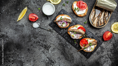 Appetizer sandwich with sprats, tomatoes and cream cheese on dark background, banner, menu recipe place for text, top view