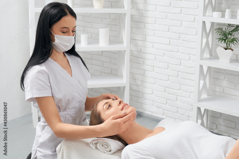 Side view of young brunette beautiful woman on procedure massage for face in beautician. Concept of special care for face and body in professional spa salon. Side view of young brunette beautiful woman on procedure massage for face in beautician. Concept of special care for face and body in professional spa salon.