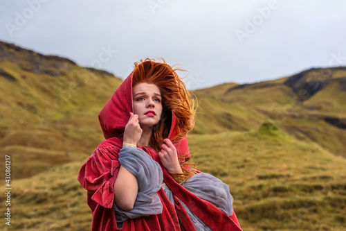 Close up photo of sad girl in old-fashioned clothes with a red cloak. Faroe Islands